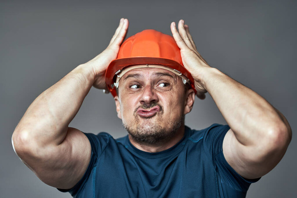 Extremely stressed engineer in hardhat against gray background - Foto, Imagen