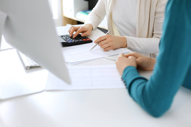 Accountant checking financial statement or counting by calculator income for tax form, hands close-up. Business woman sitting and working with colleague at the desk in office. Audit concept - Foto, afbeelding