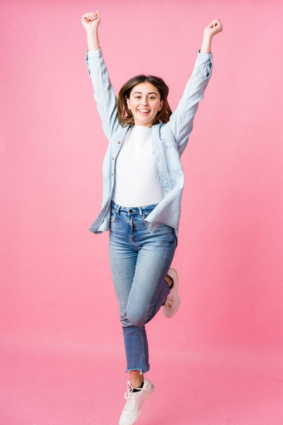 jonge vrouw springen op roze achtergrond - Foto, afbeelding