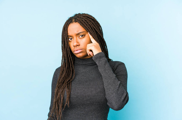 Junge afrikanisch-amerikanische Frau isoliert auf blauem Hintergrund zeigt mit dem Finger auf die Schläfe, denkt nach, konzentriert sich auf eine Aufgabe. - Foto, Bild