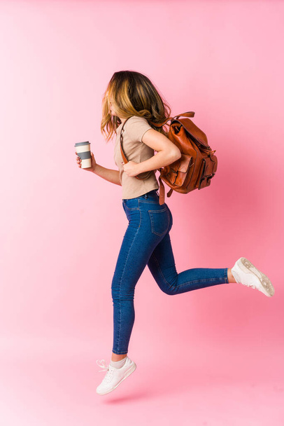 Jovem estudante caucasiano mulher saltando wih coffe no fundo rosa - Foto, Imagem