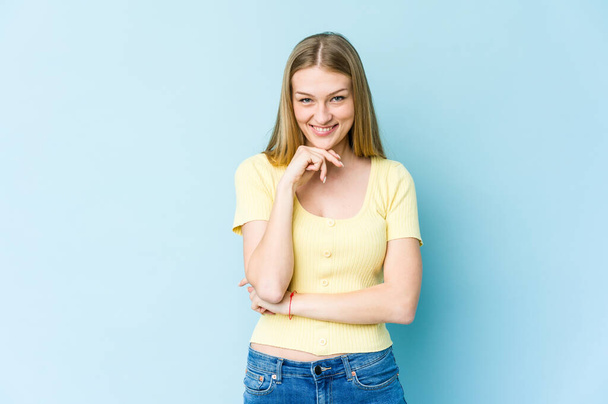 Young blonde woman isolated on blue background smiling happy and confident, touching chin with hand. - Foto, Bild
