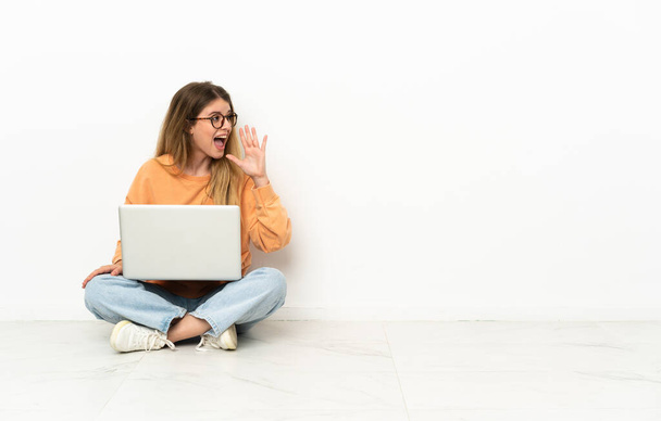 Mladá žena s laptopem sedícím na podlaze a křičícím s ústy dokořán dokořán. - Fotografie, Obrázek