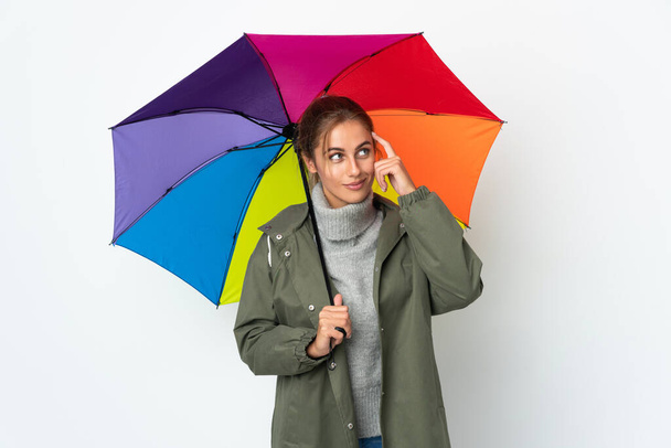 Nuori nainen, jolla on valkoisella taustalla eristetty sateenvarjo, epäilee ja ajattelee: - Valokuva, kuva