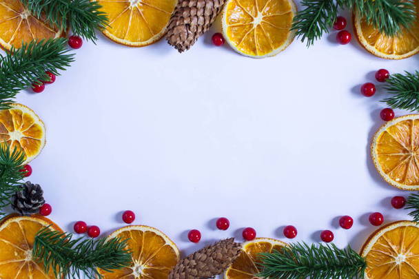 Fond blanc de Noël avec place pour le texte, branches de sapin, oranges séchées, baies rouges, glands et cônes enneigés autour des bords - Photo, image