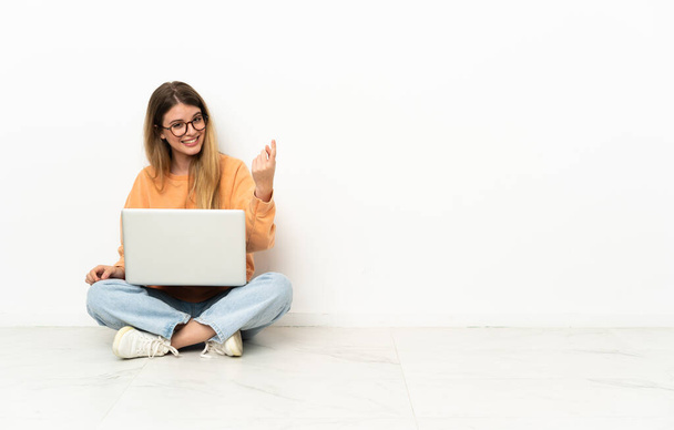 Młoda kobieta z laptopem siedząca na podłodze i wykonująca nadchodzący gest - Zdjęcie, obraz