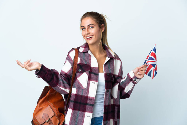 Giovane donna che tiene una bandiera del Regno Unito isolata su sfondo bianco tendendo le mani di lato per invitare a venire - Foto, immagini