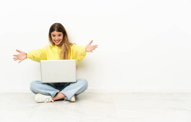jonge vrouw met een laptop zitten op de vloer presenteren en uitnodigen om te komen met de hand - Foto, afbeelding