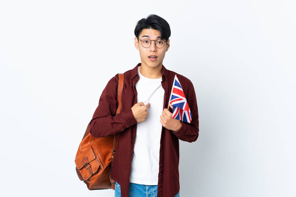 Homem chinês segurando uma bandeira do Reino Unido isolado em fundo roxo com expressão facial surpresa - Foto, Imagem