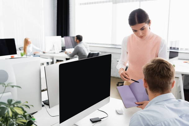 同僚とコンピュータの近くのノートパソコンを指しているビジネスマンの女性の前にぼやけた画面で  - 写真・画像