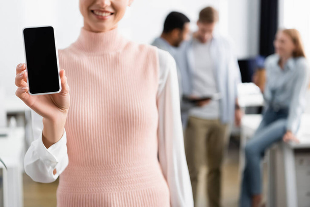 Cropped view of smiling businesswoman holding smartphone with blank screen on blurred background  - Fotografie, Obrázek