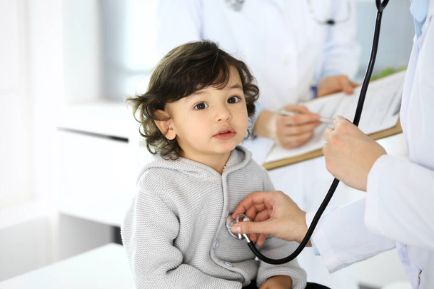 Doctor examining a child patient by stethoscope. Cute arab boy at physician appointment. Medicine and healthcare concept - Фото, изображение