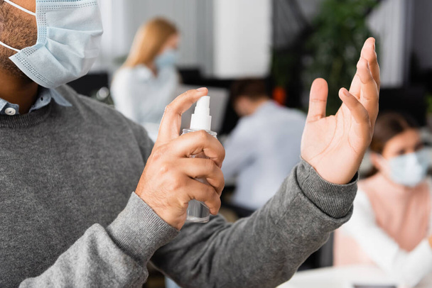 Cropped view of indian businessman in medical mask using hand sanitizer in office  - Foto, Bild