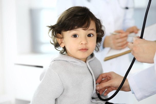 Doctor examining a child patient by stethoscope. Cute arab boy at physician appointment. Medicine and healthcare concept - Foto, Bild