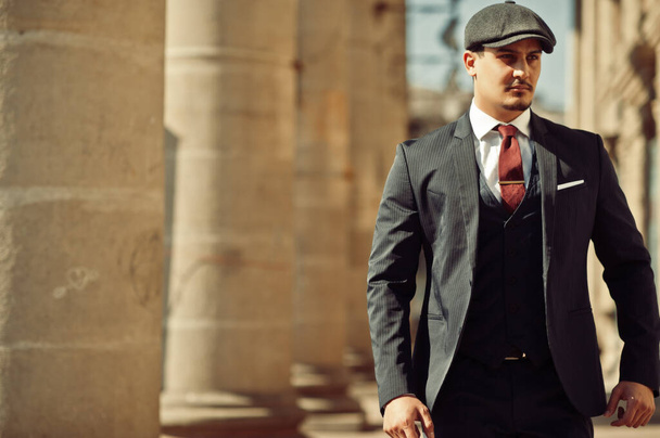 Portrait of retro 1920s english arabian business man wearing dark suit, tie and flat cap near old columns. - 写真・画像