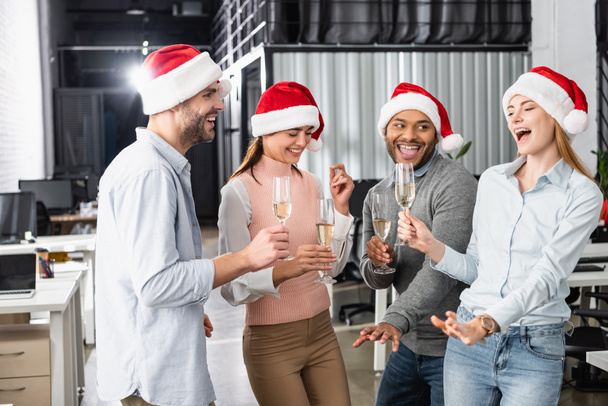 Cheerful multiethnic businesspeople in santa hats having fun with glasses of champagne in office  - Фото, зображення