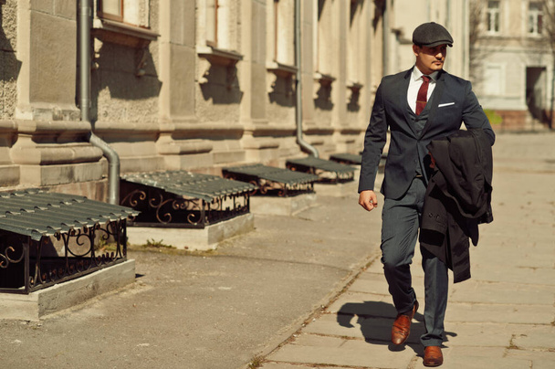 Portrait of retro 1920s english arabian business man wearing dark suit, tie and flat cap walking on old streets. - Valokuva, kuva