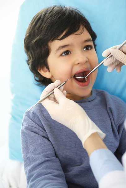 Little arab boy sitting at dental chair with open mouth during oral check up while doctor. Visiting dentist office. Medicine and stomatology concept - Photo, image