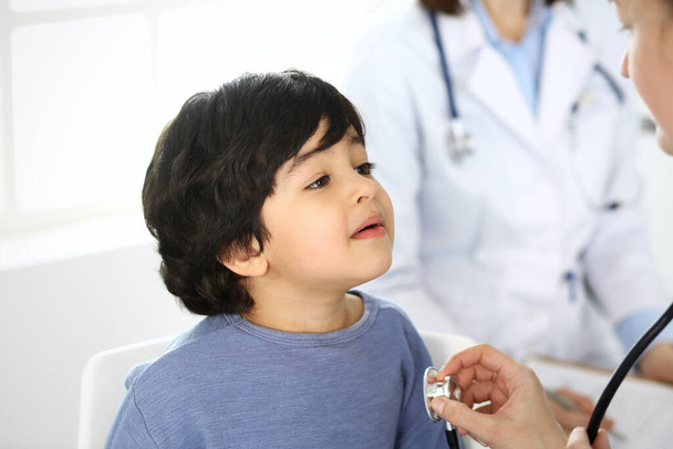 Doctor examining a child patient by stethoscope. Cute arab boy at physician appointment. Medicine and healthcare concept - Foto, immagini
