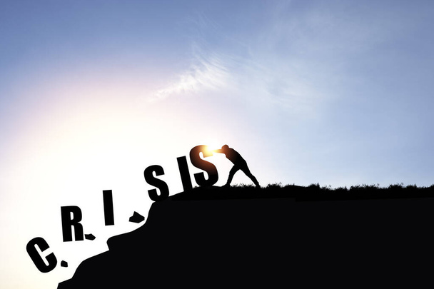 Positive thinking and mindset concept, Silhouette businessman pushing crisis wording from cliff with blue sky to eliminate it from life. - Photo, Image