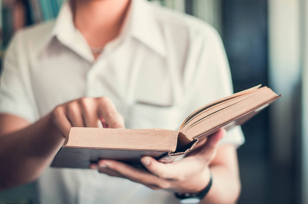 Fiatal férfiak viselnek fehér inget Egy férfi áll olvasó egyetemi könyvtár olvasás és pihenés homályos háttér, vízszintes, film hatása - Fotó, kép