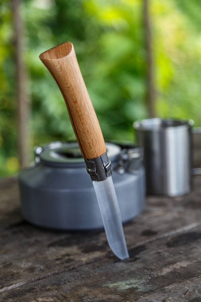 Kettle with a mug in a tourist camp. outdoor recreation in the Carpathian forest. knife and a mug on a wooden stand in outdoor. Tourist - Zdjęcie, obraz