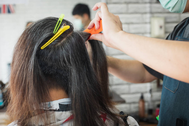 Asiático joven siendo cortado de pelo largo a pelo corto con tijera por peluquero profesional en barbería. - Foto, Imagen