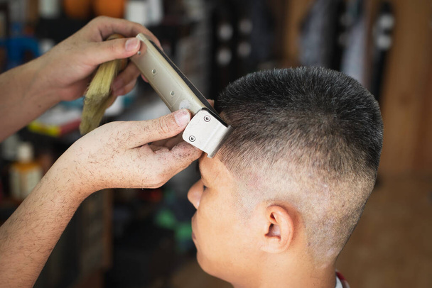 Asiatischer junger Mann mit grauen Haaren wird von einem professionellen Friseur im Friseursalon mit einem elektrischen Haarschneidegerät frisiert.  - Foto, Bild