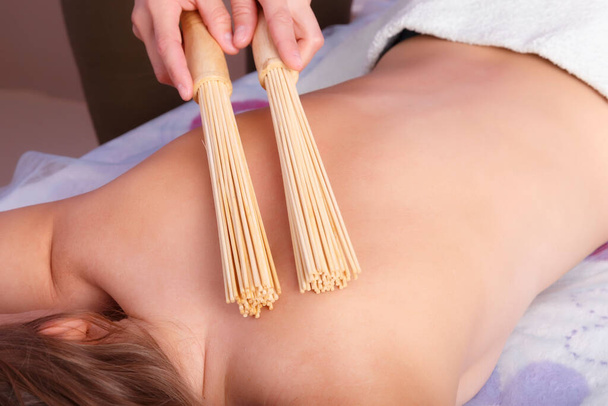 Hands of masseur with bamboo sticks doing massage of back - Foto, Imagem