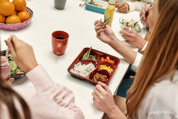 Un primer plano de un alimento saludable que consiste en verduras y arroz comiendo por una joven sentada en una mesa durante un almuerzo de negocios - Foto, imagen