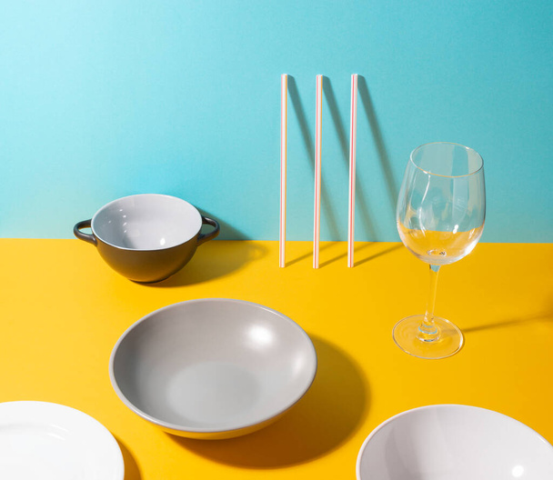 Set of assorted plates, straws and a glass on yellow and blue background - Φωτογραφία, εικόνα