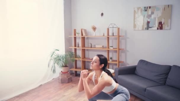 Bruneta sportovkyně dělá dřepy u gauče v obývacím pokoji - Záběry, video