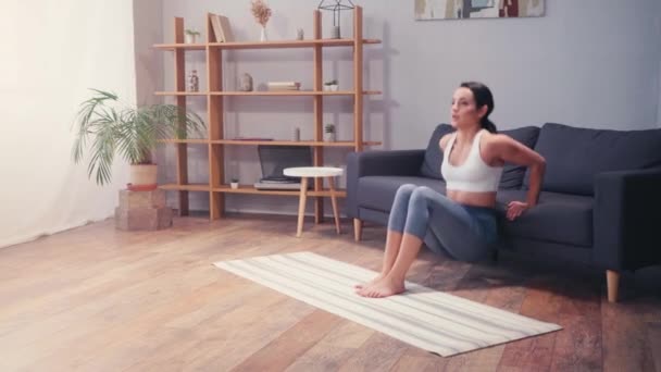 Sportnő fekvőtámaszt csinál a kanapé mellett a nappaliban  - Felvétel, videó