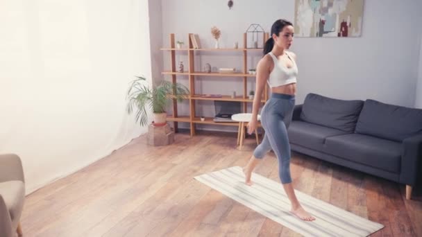 Mezítlábas sportolók guggolnak a fitnessz szőnyegen a nappaliban  - Felvétel, videó