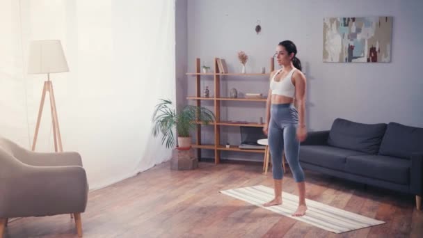 Sportiva a piedi nudi che fa salti sul tappeto fitness in soggiorno  - Filmati, video
