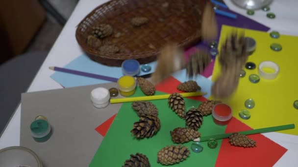 Borovicové šišky padají na stůl se školními potřebami, tužkami, barevným papírem. Art - Záběry, video
