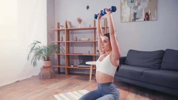 Young sportswoman training with dumbbells on fitness mat  - Záběry, video