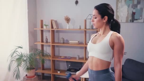 Deportista morena haciendo ejercicio con pesas en la sala de estar  - Metraje, vídeo