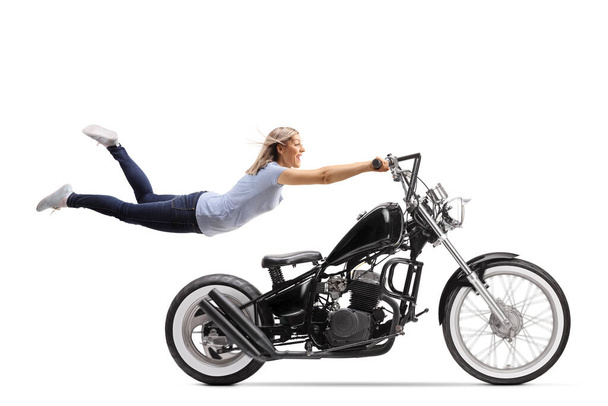 Young woman flying and holding on to a black chopper motorbike isolated on white background - Zdjęcie, obraz