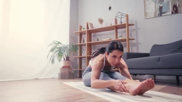 Bruneta sportovkyně protahování nohy na fitness podložku doma  - Záběry, video