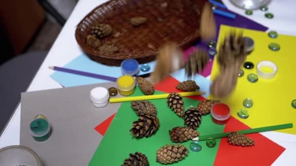 Tannenzapfen fallen auf den Tisch mit Schulbedarf, Bleistiften, buntem Papier. Kunst - Filmmaterial, Video