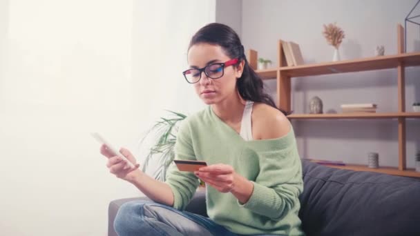 Mladá žena pomocí smartphone a kreditní karty doma  - Záběry, video