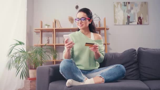 Fröhliche Frau mit Kreditkarte und Smartphone zu Hause  - Filmmaterial, Video