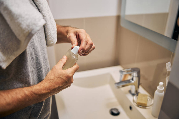 Mann öffnet im Badezimmer eine Flasche mit einer Körperwäsche - Foto, Bild