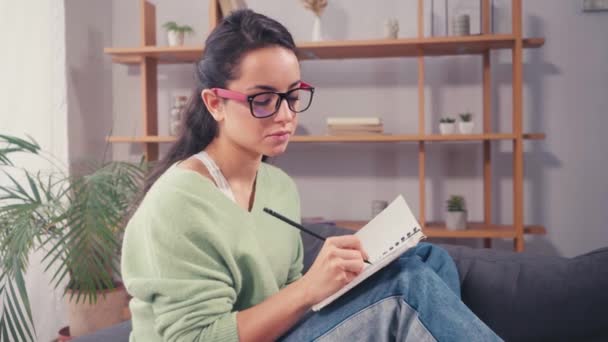 Μαθητής με γυαλιά που γράφει στο σημειωματάριο στο σπίτι  - Πλάνα, βίντεο