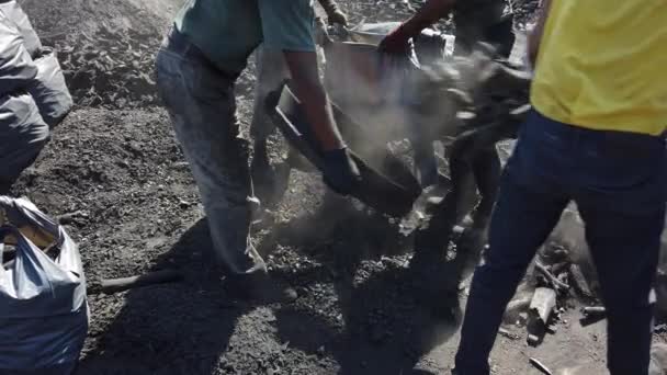 hommes en vêtements sales tamiser à travers les grumes brûlées bois de chauffage emballage de charbon dans des sacs - Séquence, vidéo