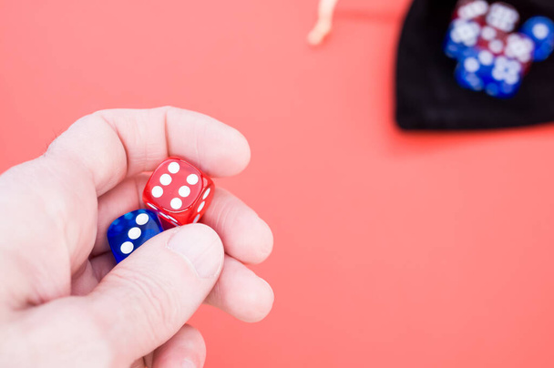 A closeup shot of a hand holding red and blue dice isolated on light orange background - Foto, immagini