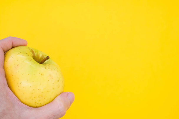 A closeup shot of a hand holding a yellow apple isolated on yellow background - Valokuva, kuva