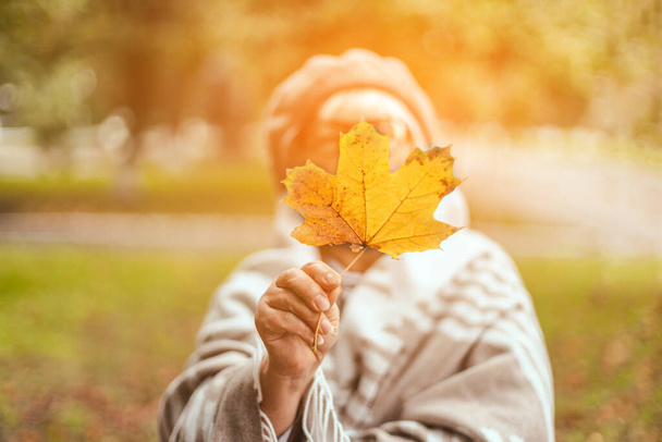 Mulher loira caucasiana feliz sob cobertor de malha quente andando no parque de outono. Retrato de menina com folha de outono amarelo em um parque de outono ensolarado - Foto, Imagem
