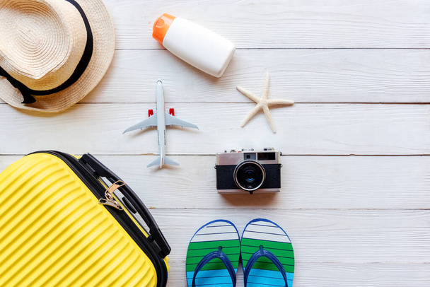 Top View Summer Travel and Plan.  Yellow suitcase luggage with accessories fashion, old camera, sunblock . Travel in the holiday trips airplane on wood white background in holiday trips.   Summer and Travel Concept - Photo, Image